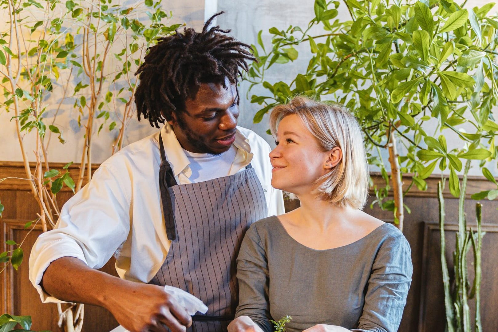 Happy interracial couple watering a plant together, staring lovingly at each other while they water the plant. Photo by Antoni Shkraba